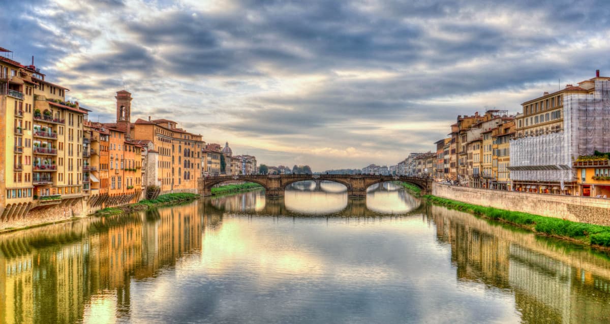 The Ponte Santa Trinita bridge reflected in the Arno river at sunset in Florence