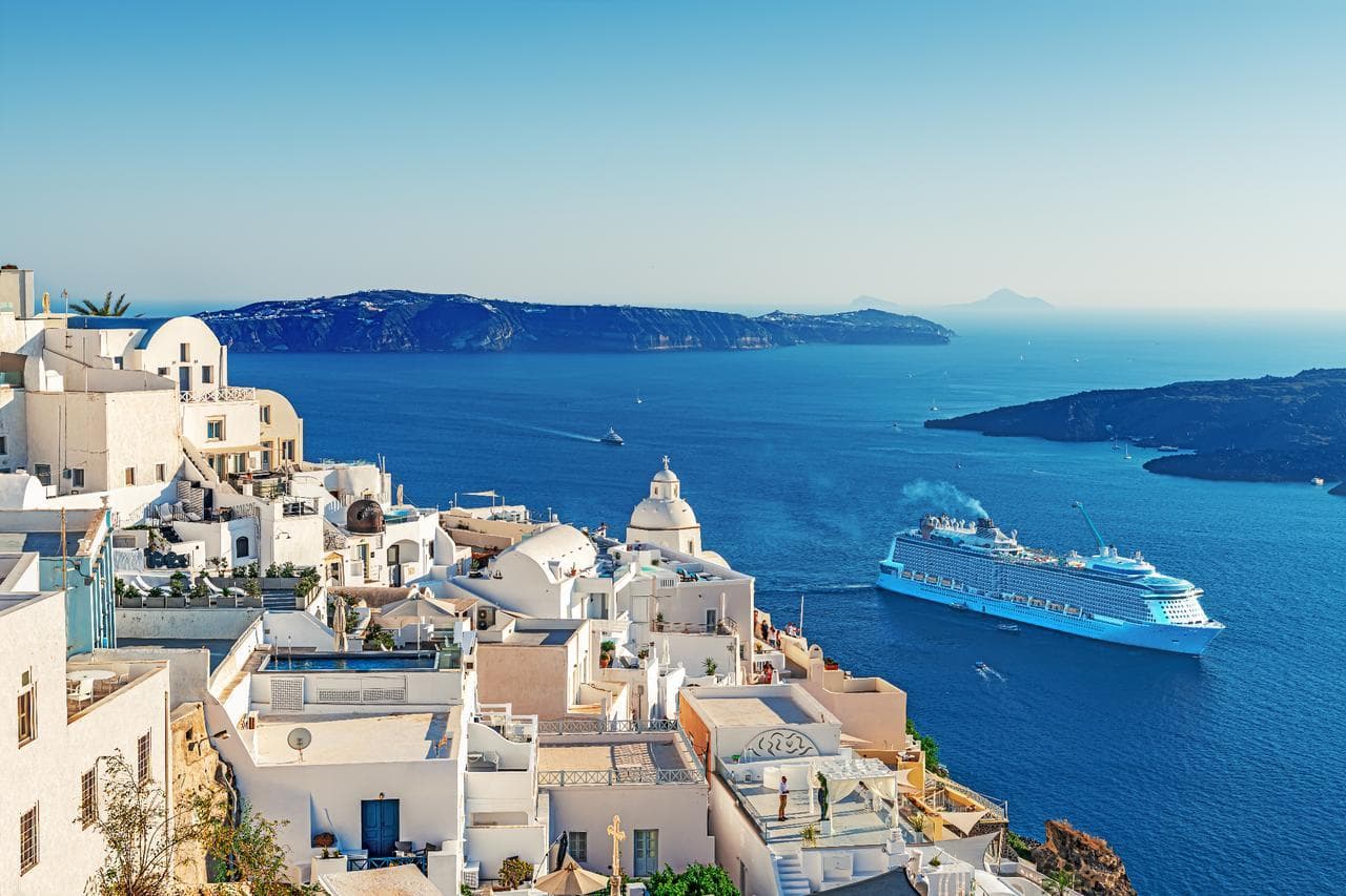 A cruise ship passing below the white clifftop villages of Santorini in the Mediterranean