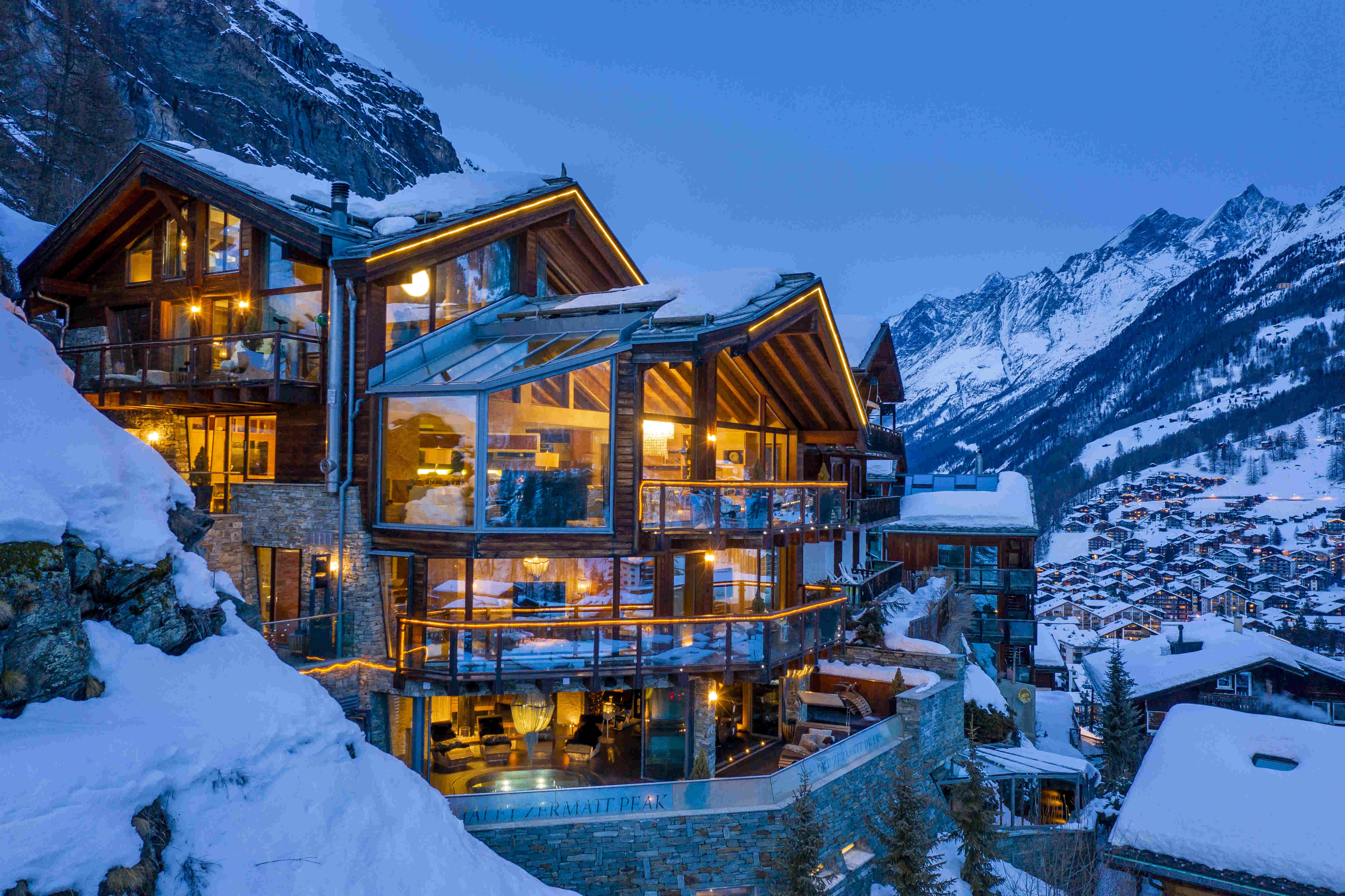 A luxury alpine chalet glowing at dusk above the lights of Zermatt, with snow-capped peaks behind