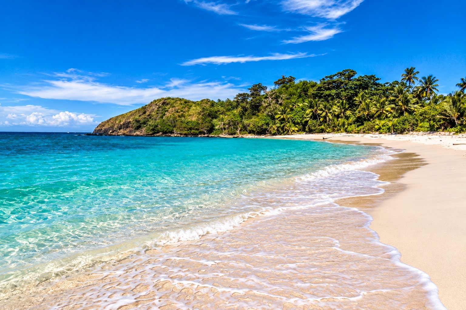 Turquoise water meeting a white-sand beach beside a palm-covered headland in Fiji