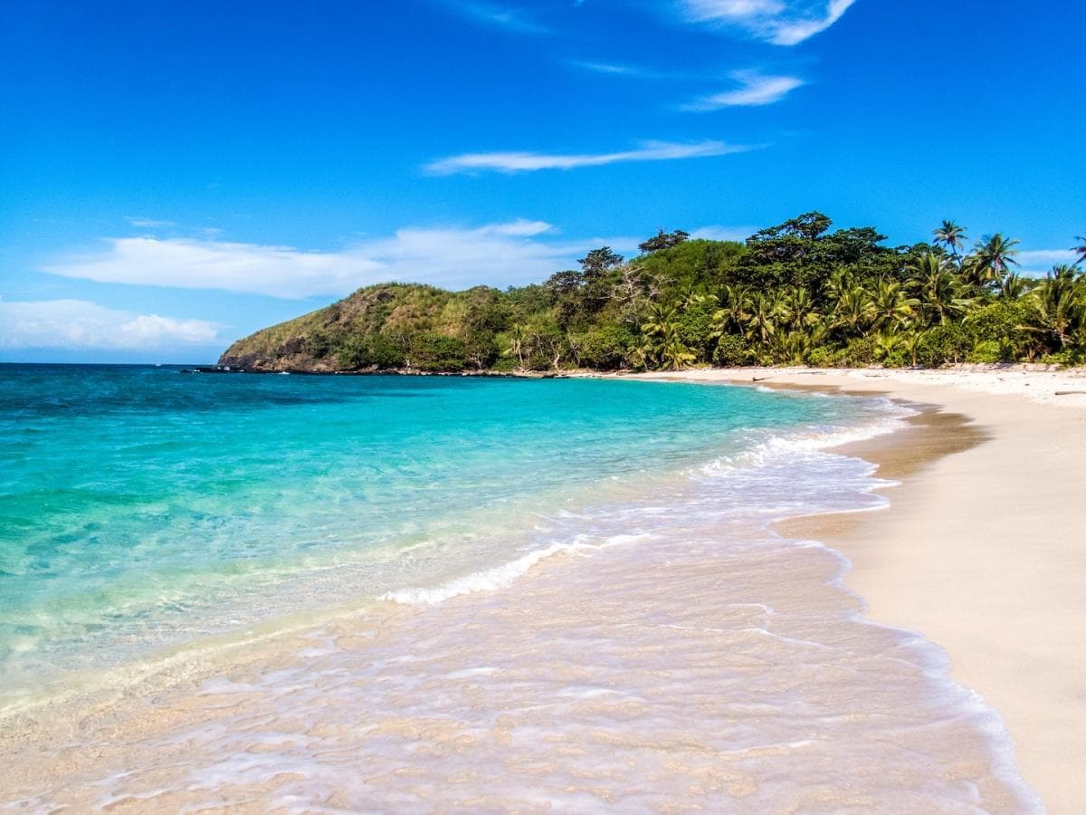 Turquoise water meeting a white-sand beach beside a palm-covered headland in Fiji