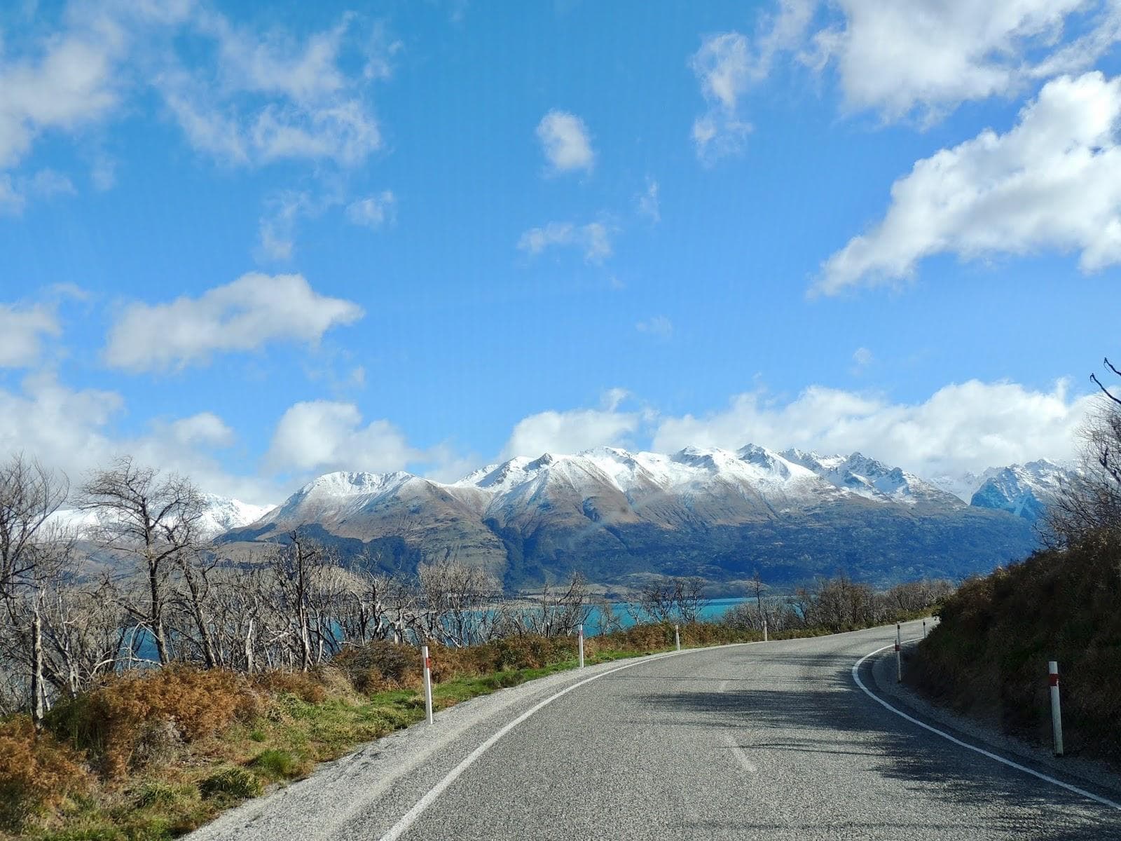 A winding country road above a turquoise lake, framed by snow-capped mountains near Glenorchy