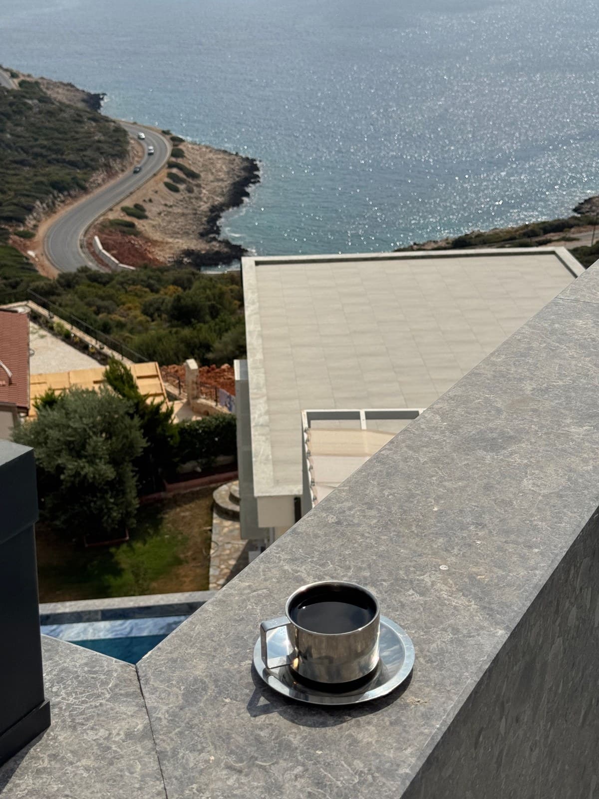 Coffee cup on a stone balcony ledge overlooking the sea and a winding coastal road