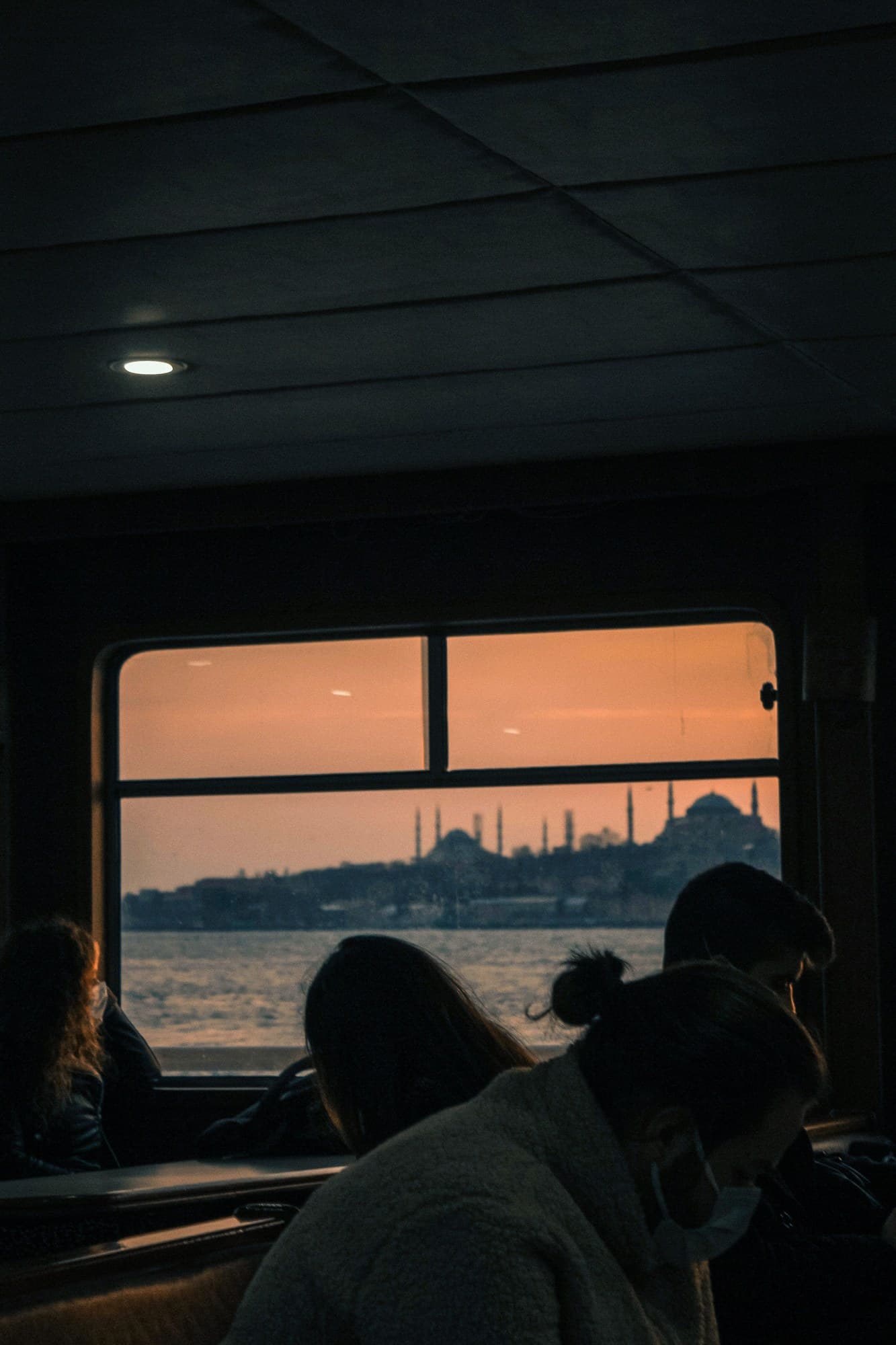 Passengers silhouetted against a train window overlooking the Istanbul skyline at sunset