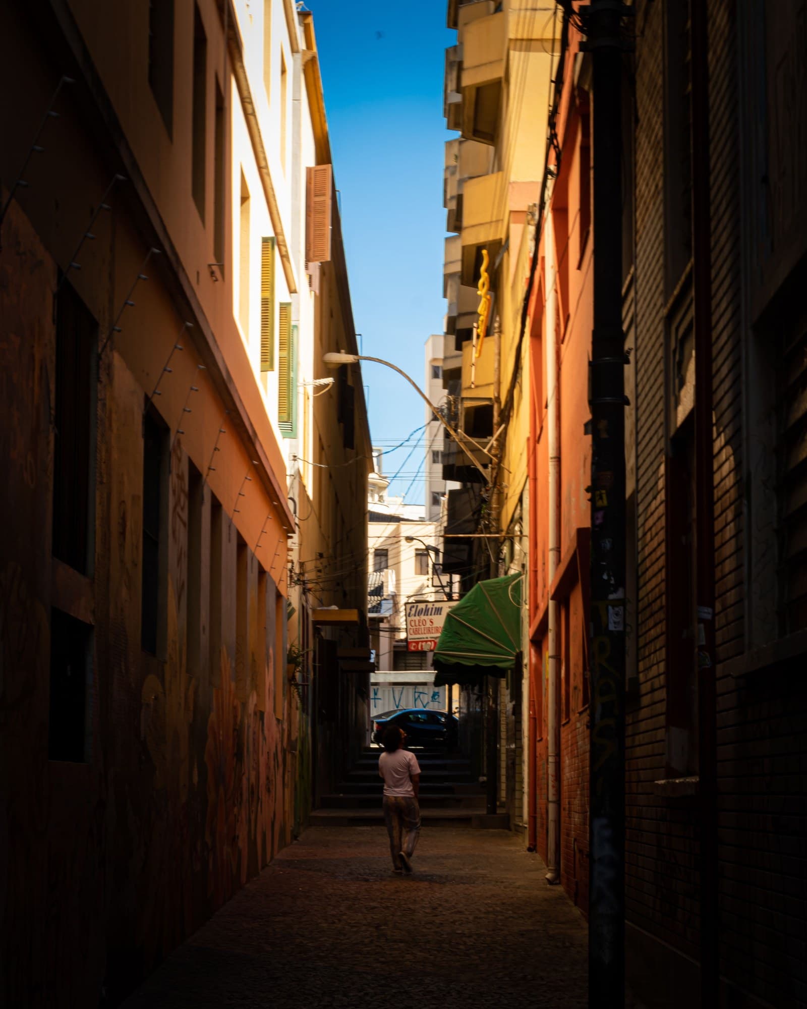 Traveler walking away down a narrow, sunlit historic street, seen from behind